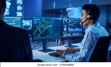 Confident Male Data Scientist Works on Personal Computer Wearing a Headset in Big Infrastructure Control and Monitoring Room. Map Surveillance of People Walking on City Streets - Shutterstock ID 1798108984