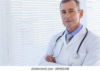 Confident Male Doctor Looking At Camera With Arms Crossed In Medical Office