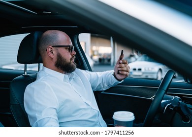 Confident Male Driver In Optical Spectacles For Provide Eyes Protection Concentrated On Smartphone Using While Testing Autopilot Self-driving In Advanced Expensive Automobile, Transportation Concept