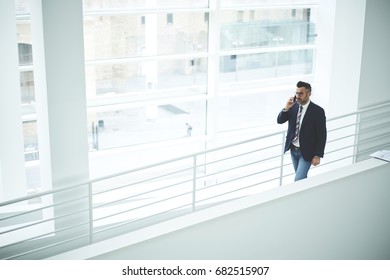 Confident Male Entrepreneur Dressed In Formal Outfit Walking On Stairs In White Interior Office Building, Experienced Matured Executive Manager Talking On Mobile Phone Having Business Conversation