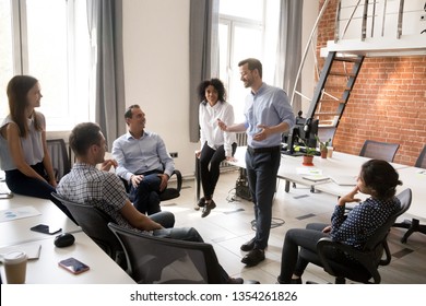 Confident male leader, coach talking with multiracial group of office workers, having good conversation with subordinate, brainstorming, discussing business strategy, ideas, team building activity