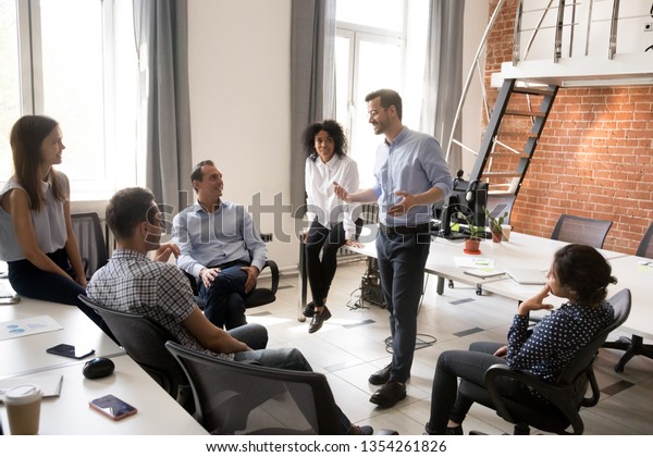 Confident male leader, coach talking with\
multiracial group of office workers, having good conversation with\
subordinate, brainstorming, discussing business strategy, ideas,\
team building\
activity