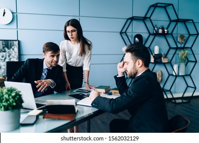 Confident Male Manager Business Clothes Using Laptop And Setting Task For Office Workers While Concentrated Male Making Notes And Female Looking At Screen At Stylish Office 