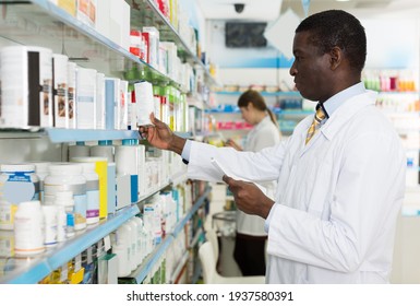 Confident male pharmacist working in drugstore, picking up prescription medicines on shelves