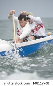 Confident Male Rowers Paddling Outrigger Canoe In Race