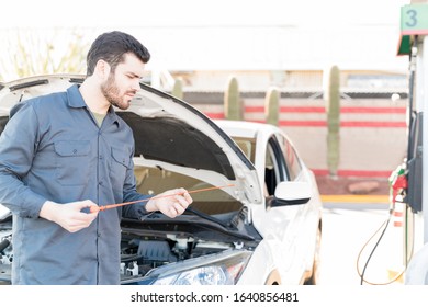 Confident male worker checking engine oil with dipstick at gas station