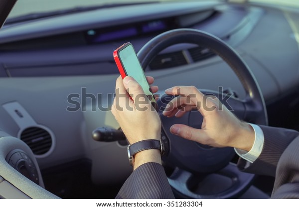Confident man in a business suit in the driver\'s\
seat holding a touchscreen phone or navigator. Businessman sitting\
in the car takes a business\
call.