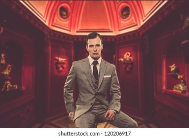 Confident Man In Classic Grey Suit Sitting On Chair In Cabinet