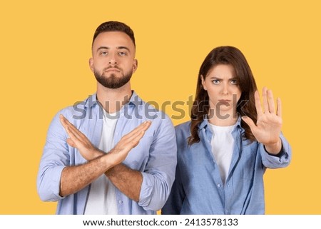 Confident man crossing arms to signal no and serious woman with hand outstretched in stop gesture, both indicating denial or refusal against bright yellow backdrop