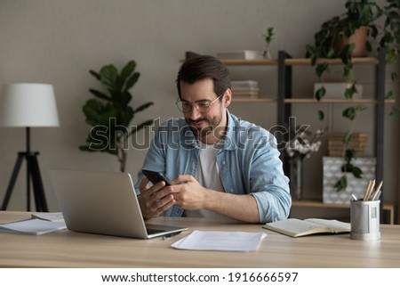 Confident man sitting at desk taking break in work with electronic documents on laptop to make answer telephone call. Smiling young guy freelancer synchronize data between home computer and smartphone ストックフォト © 