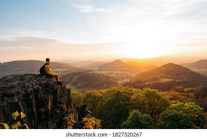 Confident man sitting on the edge. Amazing view  in hilly landscape far from people. Tourist student is relaxing in nature during sunset. Traveling sitting in mountains. Adventure, Art, Travel and Hike concept.