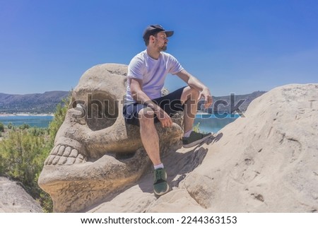 Confident man sitting on a skull shaped stone. Incredible route with sculptures carved in the rocks, a hiking route in the vicinity of the Buendia reservoir. Man enjoying the relaxed landscape. Cuenca