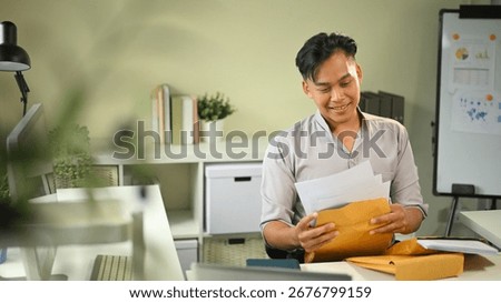 Confident man sorting documents from a folder in a modern workspace