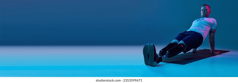 Confident man in sport uniform with prosthetic legs doing plank in horizontal position in neon light on floor. Motivation poster. Concept of sport for people with disabilities, medical, health. banner - Powered by Shutterstock