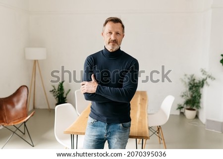 Confident man standing with folded arms scrutinising at the camera with an intense stare and sombre thoughtful expression