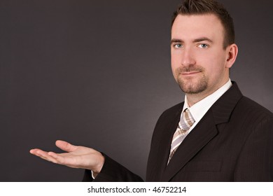 Confident Man In Suit Looking At Camera With Hand Open, On Dark Background