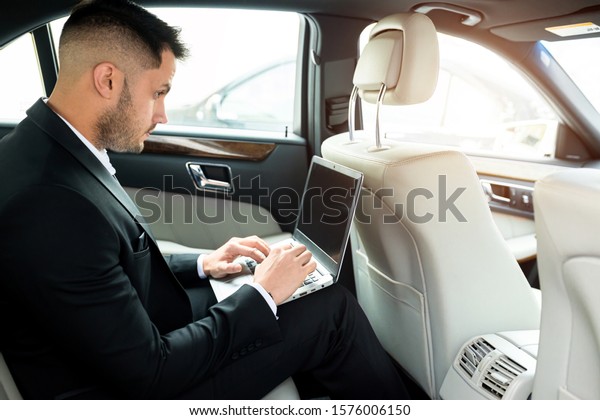 Confident man in tuxedo sit using laptop, working\
in car, man with\
beard