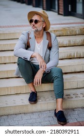 Confident Man Wearing Straw Hat And Backpack Sitting On Stairs, Businessman In Casual Clothes In Summer On The Way To Work.