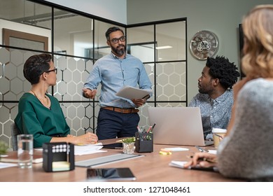 Confident mature businessman giving a presentation to his team in office. Business brief with annual goals with employees and mature boss in meeting room. Multiethnic leader training business people.