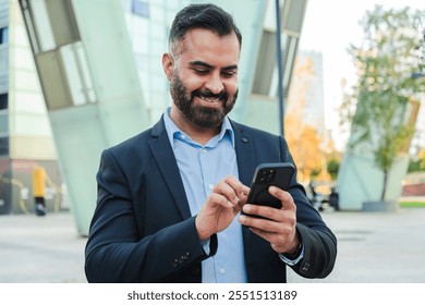 Confident mature businessman using a cellphone outdoors in a modern cityscape, wearing formal suit, smiling and staying productive, showcasing professional success, communication, and connectivity - Powered by Shutterstock