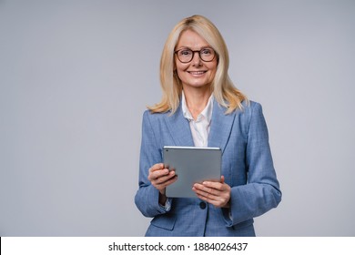 Confident mature caucasian business woman holding a tablet in formal suit isolated over grey background - Powered by Shutterstock