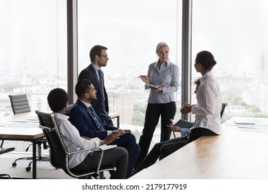 Confident mature female business leader holding meeting, training, coaching with diverse team of new employees. Senior mentor teaching interns sitting in circle in open office space - Powered by Shutterstock