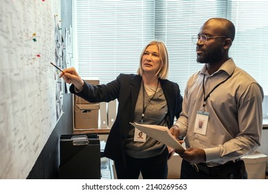 Confident mature female FBI agent pointing at map while showing male colleague possible locations of criminal at meeting