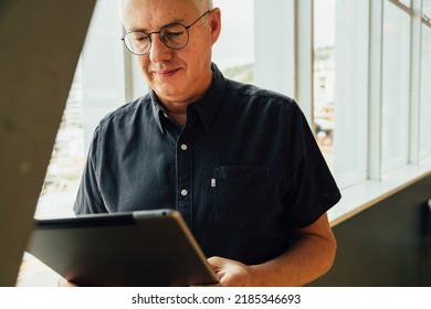 Confident Mature Male Executive Analyzing Business Data Over Digital Tablet While Standing By Window In Office