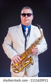 Confident Mature Male Saxophonist Posing With Instrument In White Suit And Sunglasses. Against Black Background.Vertical Image