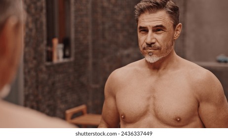 Confident mature male standing shirtless in front of a bathroom mirror. Portrait of muscular fit aged man, smiling. - Powered by Shutterstock