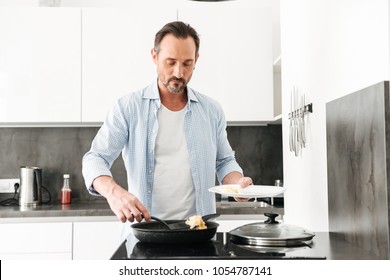 Confident Mature Man Cooking Breakfast While Standing At The Kitchen At Home