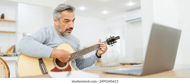 Confident mature man engaging with guitar lessons online, focused and expressive in a modern kitchen setting. - Powered by Shutterstock