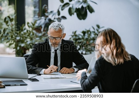 Confident mature man in formalwear interviewing job candidate while sitting at the desk in office