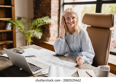 Confident mature middle-aged architect engineer talking on smartphone with clients boss, working on architectural plans, drawing new projects in office - Powered by Shutterstock