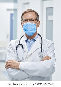 Confident Mature Old Medical Health Care Professional Doctor Wearing White Coat, Stethoscope, Face Mask Standing In Hospital Looking At Camera. Medical Staff Health Care Protection Concept. Portrait