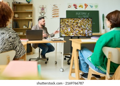 Confident Mature Teacher Telling Group Of Highschool Students About Life Of Bees While Making Presentation On Interactive Screen