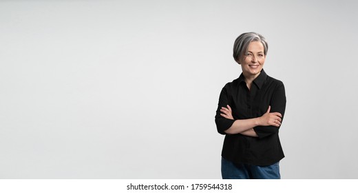 Confident mature woman smiling arms crossed. Gray haired businesswoman in black shirt on white background. Horizontal template for ad banner with copy spase for text.