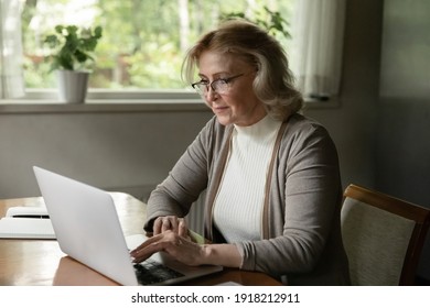 Confident Mature Woman Wearing Glasses Using Laptop, Browsing Apps, Searching Information In Internet, Shopping Or Chatting Online, Reading News, Enjoying Leisure Time With Gadget At Home