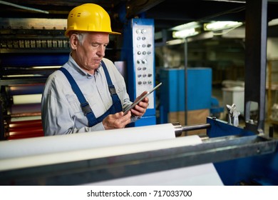 Confident mature worker wearing hardhat and overall using digital tablet white taking inventory at production department of modern plant - Powered by Shutterstock