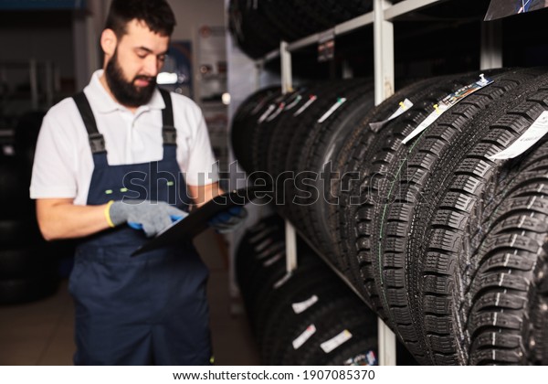 confident meachanic man during work, focus on\
tires at the repair garage. replacement of winter and summer tires.\
seasonal tire replacement\
concept.