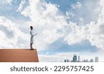 Confident medical industry employee in white suit standing at the top of building roof and holding tablet in hands. Skyscape and city view on background. Medical sphere concept