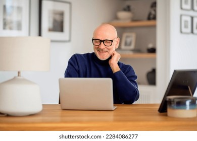 Confident middle aged man using laptop and having video call while working from home. Confident male wearing glasses and casual clothes. Home office.