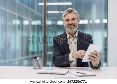 Confident middle-aged professional using a tablet at a modern office desk with joy. Portrays thoughtfulness, technology use, and the workplace environment, conveying professionalism