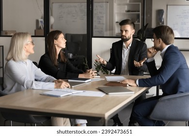 Confident motivated team leader man speaking to employees on meeting, explaining idea for project development, giving work tasks. Colleagues listening to boss, discussing collaboration - Powered by Shutterstock