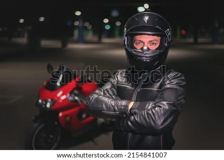 Confident motor biker man in the helmet stand at night parking.