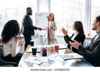 Confident multiethnic business people are shaking hands on briefing meeting in modern office. Successful business teams coming to agreetment after negotiations, coworking concept