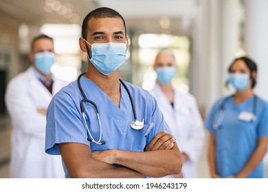 Zuversichtliche, multiethnische männliche Krankenschwester vor seinem medizinischen Team, die Kamera mit Gesichtsmaske während des Covid-19-Ausbruchs zu sehen. Glücklicher und stolzer indischer junger Chirurg, der vor seinen Kollegen steht.