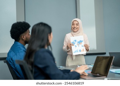 Confident Muslim woman in hijab presenting a world map and data charts to her diverse team during a meeting in an office. - Powered by Shutterstock