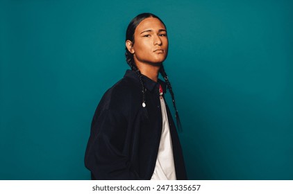Confident Native American man with braided hair stands against a blue background. Casual yet stylish, he exudes self-confidence. A captivating portrait capturing his strong presence and heritage.