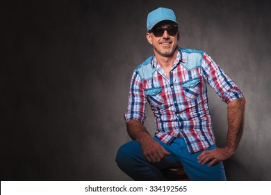 Confident Old Casual Man With Baseball Hat And Sunglassed Sitting And Looks Away From Hte Camera